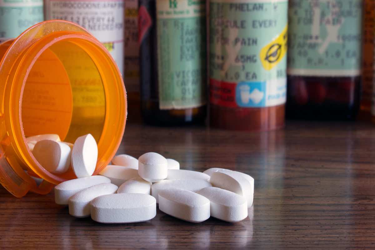 Prescription opioids with many bottles of pills in the background.