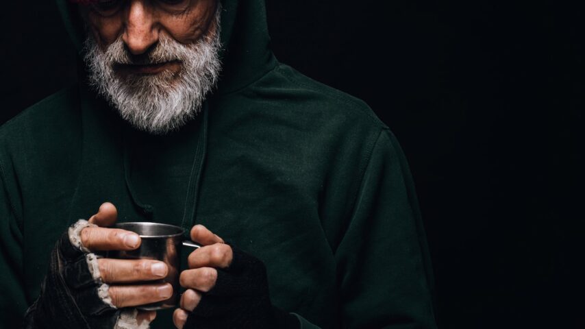 Old veteran with grey beard holding a mug of hot tea to warm himself in Arizona rehab center
