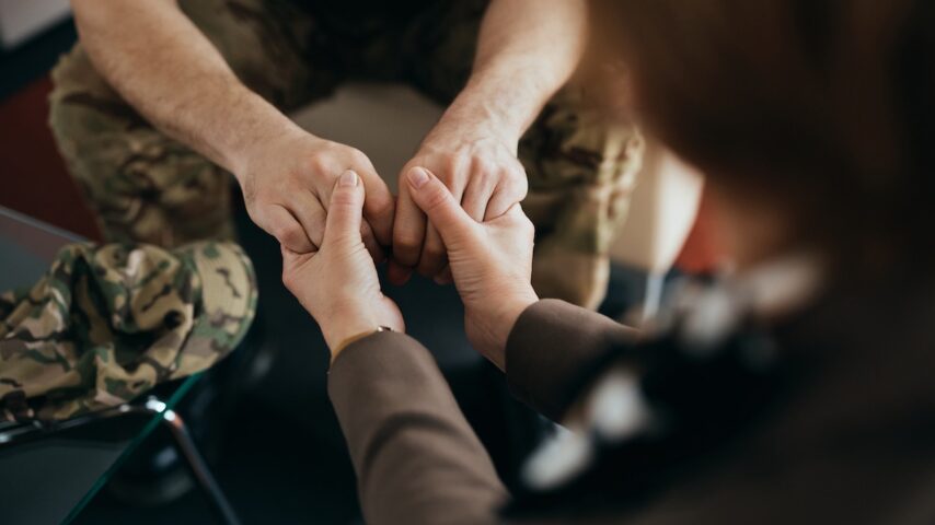 Close up of psychotherapist holding hands with soldier during counseling at her office in Virginia