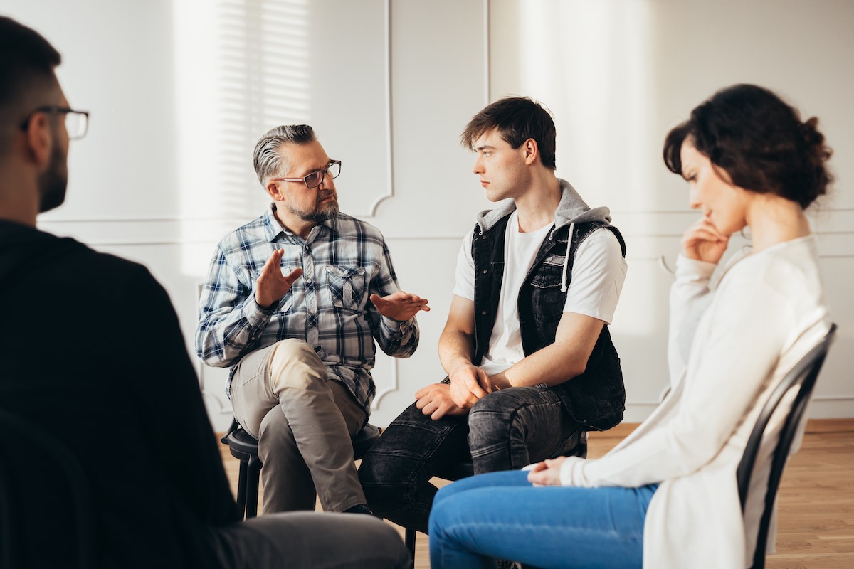Psychologist talking about 12-step program to addicted man during group support meeting