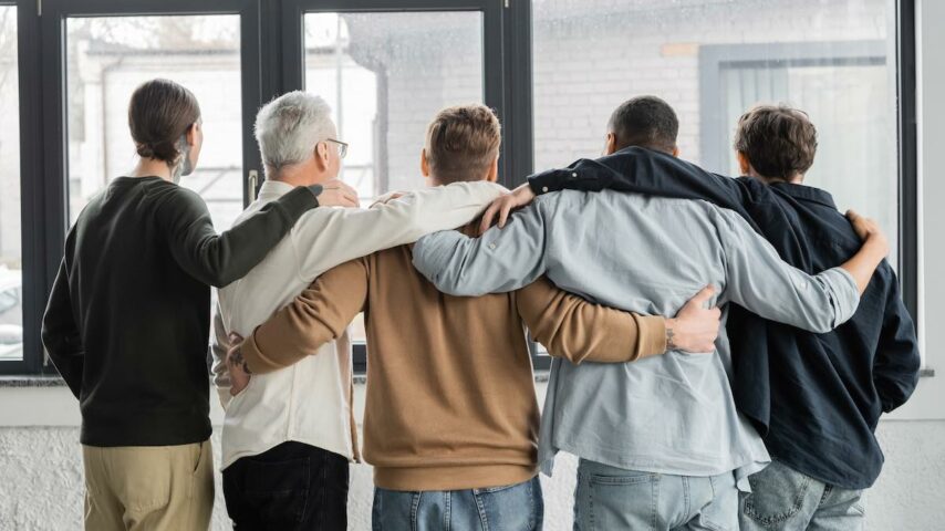 Back view of interracial men with alcohol addiction hugging in a Montana rehab center