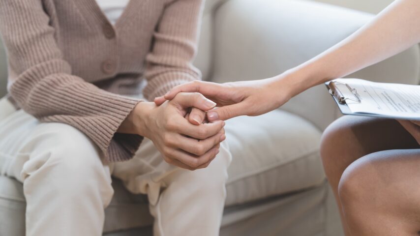 Psychologist touching hands and encouraging stressed woman about mental health problem and addiction