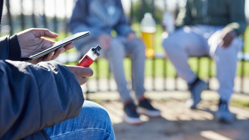Close Up of man with mobile phone and vaping in a park