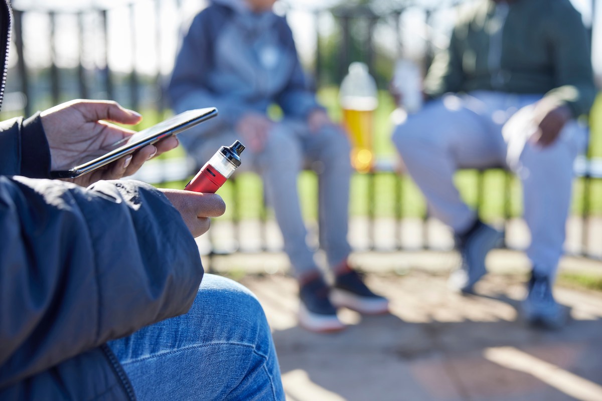 Close Up of man with mobile phone and vaping in a park