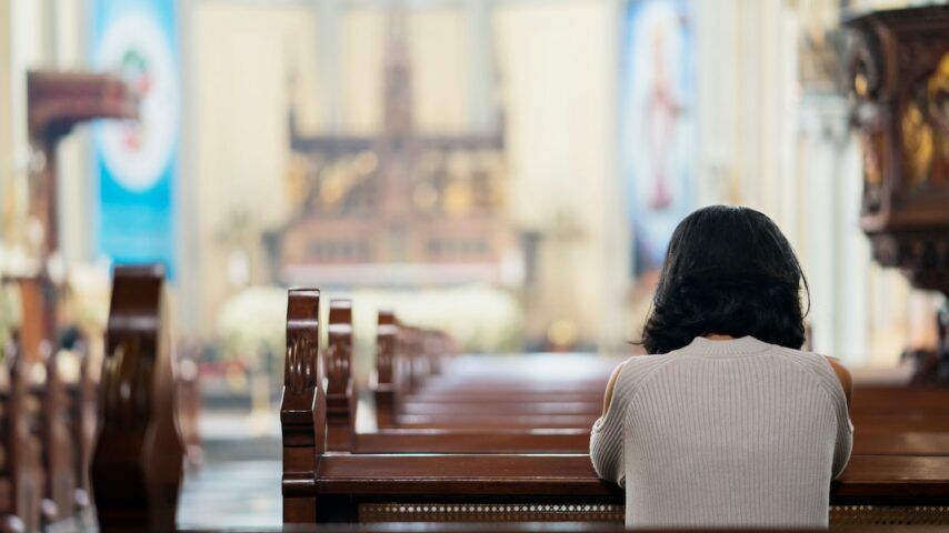 Rear view of catholic woman praying for her recovery journey in the church