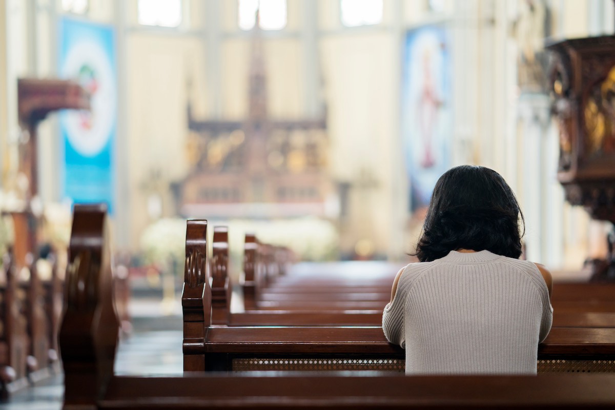 Rear view of catholic woman praying for her recovery journey in the church
