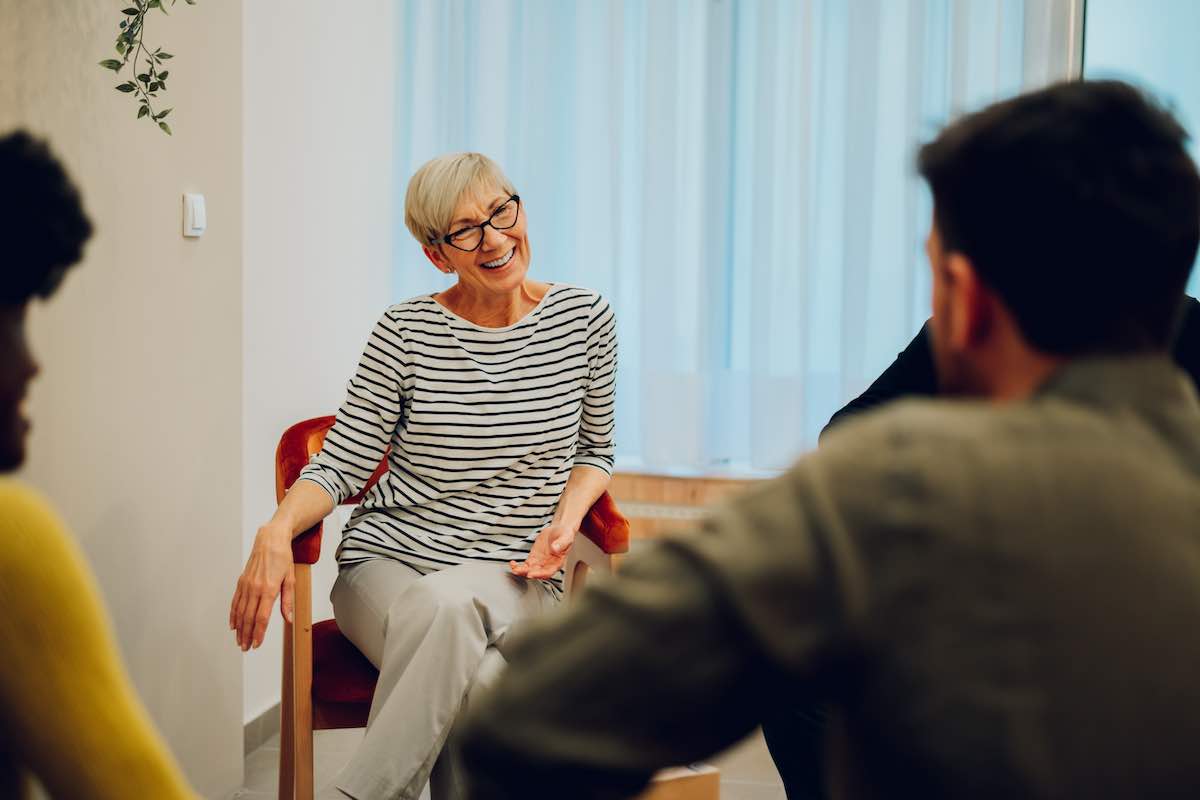 Diverse men and women at support group meeting listen to mature woman tell her ketamine rehab story